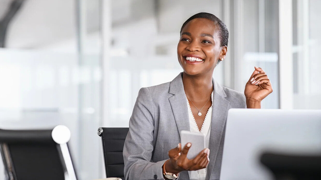 Jeune femme souriante devant un ordinateur portable et utilisant un smartphone